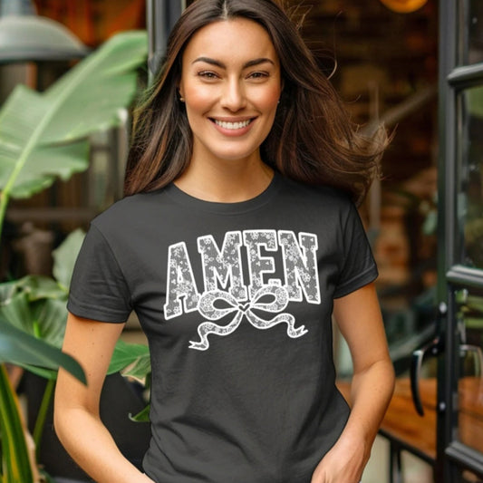 Woman wearing a black t-shirt with 'AMEN' printed on it, standing outdoors.