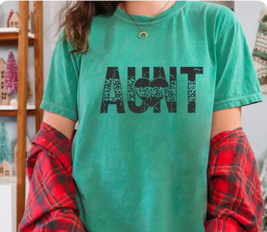 Person wearing a green t-shirt with 'Aunt' printed on it, standing indoors.