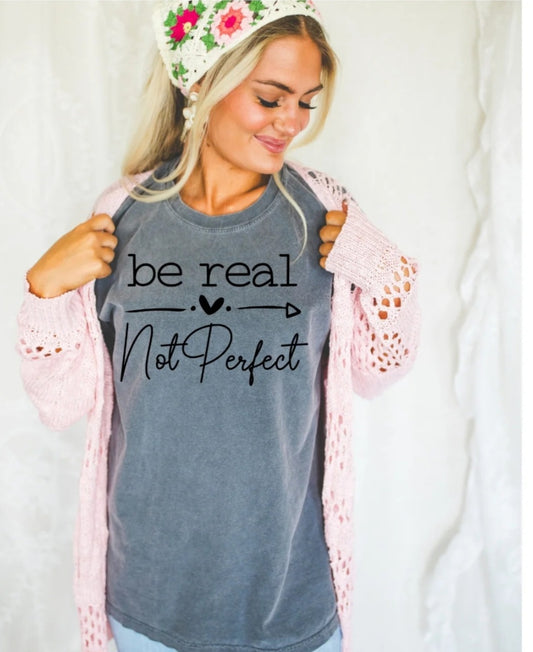 Woman wearing a gray t-shirt with 'be real not perfect' text, holding a pink lace garment.