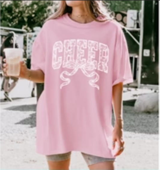Person wearing a pink 'CHEER' t-shirt with crossed pom-poms outdoors.